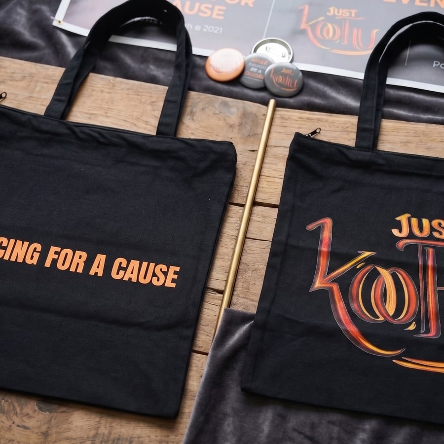 Black Just Koothu canvas tote bags with Dancing for a Cause and logo designs on a wooden surface.